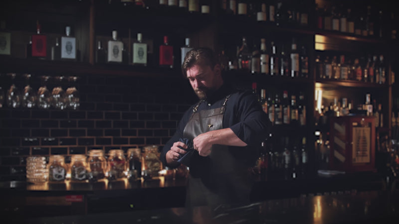 Professional bartender in a rustic bar environment working on a cocktail.