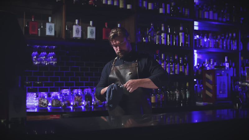 Mixologist in a dimly lit bar setting carefully crafting a cocktail.