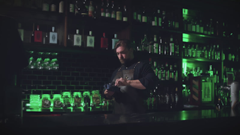 Professional bartender in a rustic bar environment working on a cocktail.