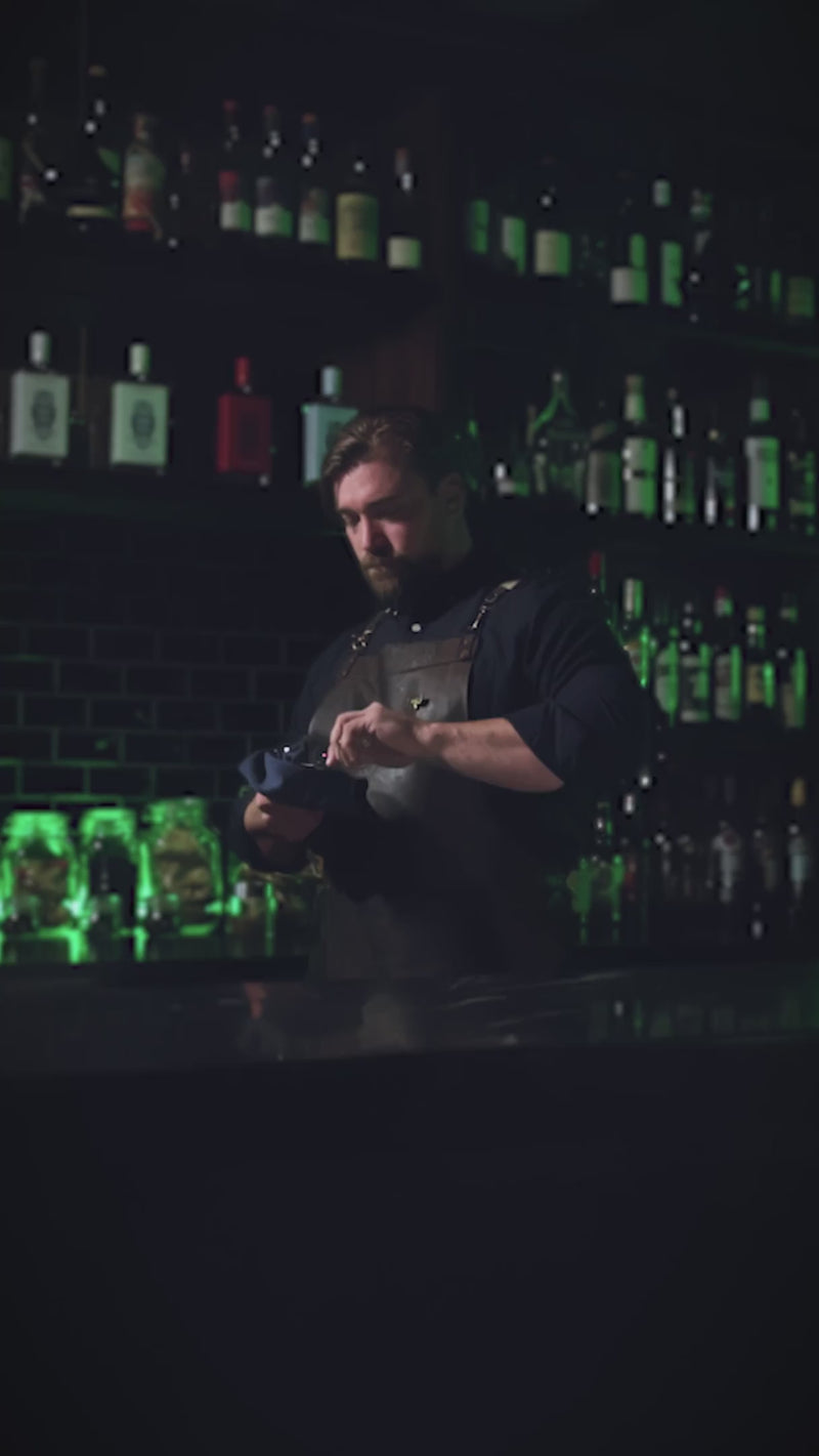 Mixologist in a dimly lit bar setting carefully crafting a cocktail.